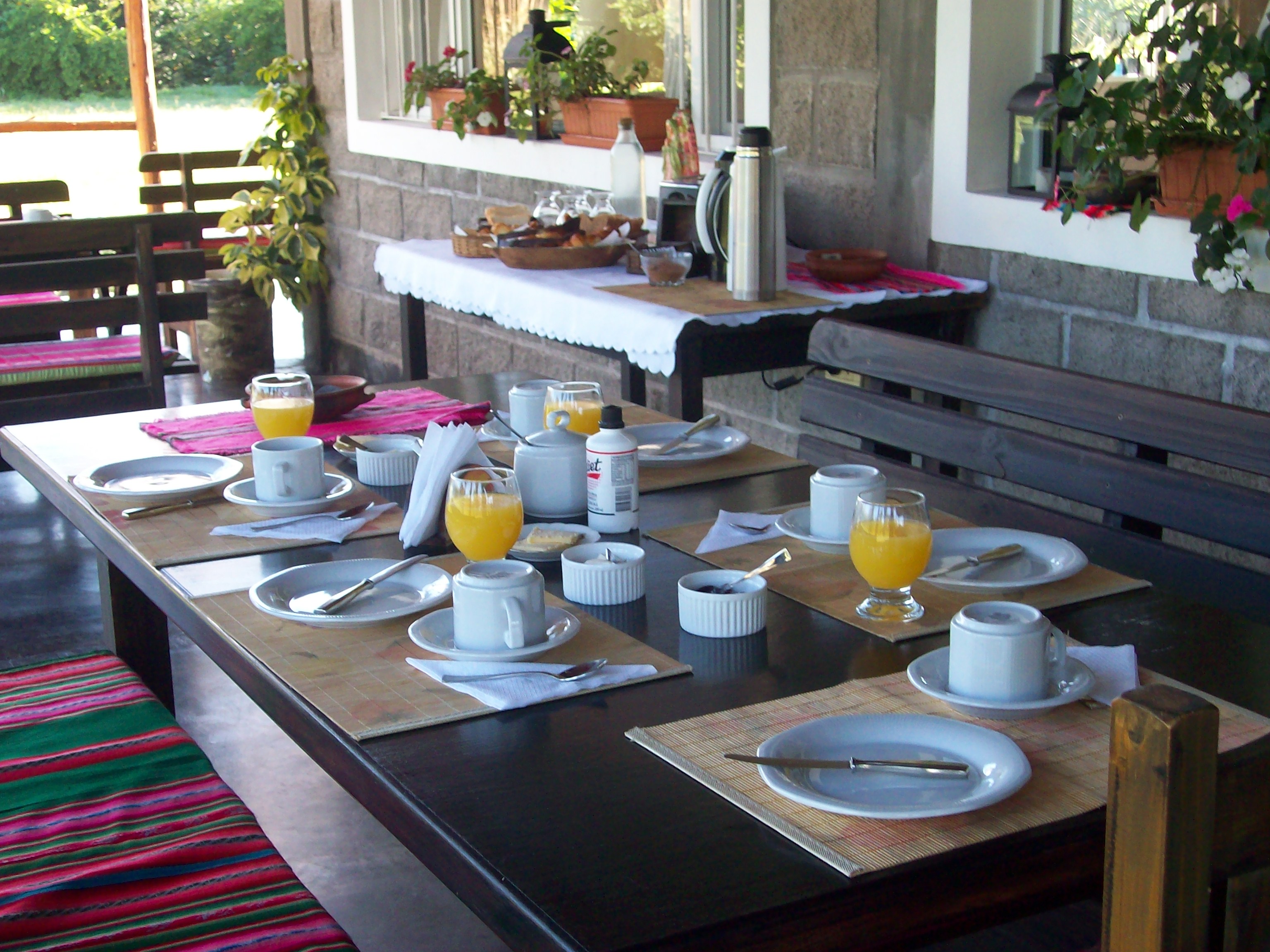 Desayuno casero servido en la galería con jugo de naranja y café - Finca La Vertiente Salta